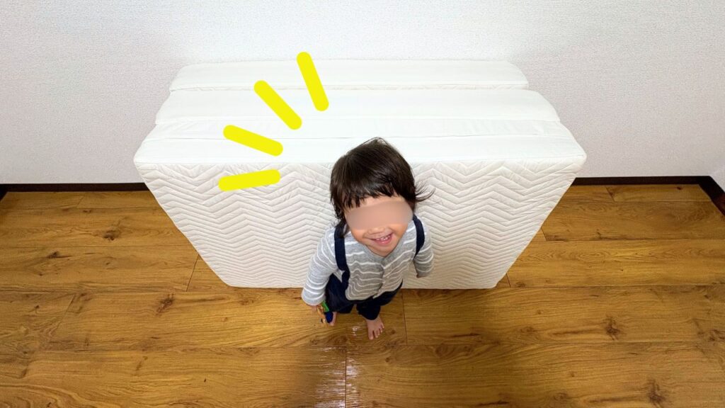 マットレスの前で笑顔を見せる１歳息子の画像